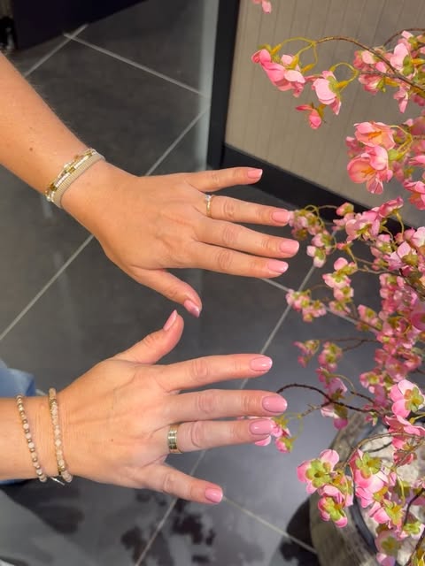 Handen met zachtroze gellak nagels bij roze bloesemtakken