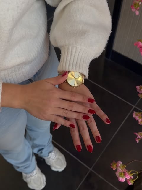 Hand met dieprode gellak nagels, witte mouw en gouden horloge